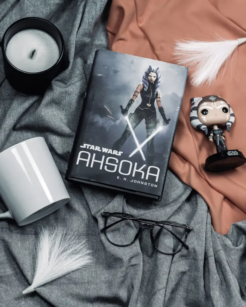 Ahsoka, the novel, by E. K. Johnston on a flat lay with tea, glasses, a candle, and an Ahsoka Tano Funko POP.